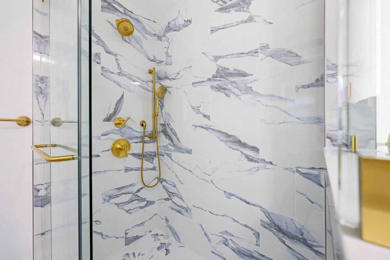 walk-in shower clad in dramatic blue-veined marble tile with brushed gold fixtures