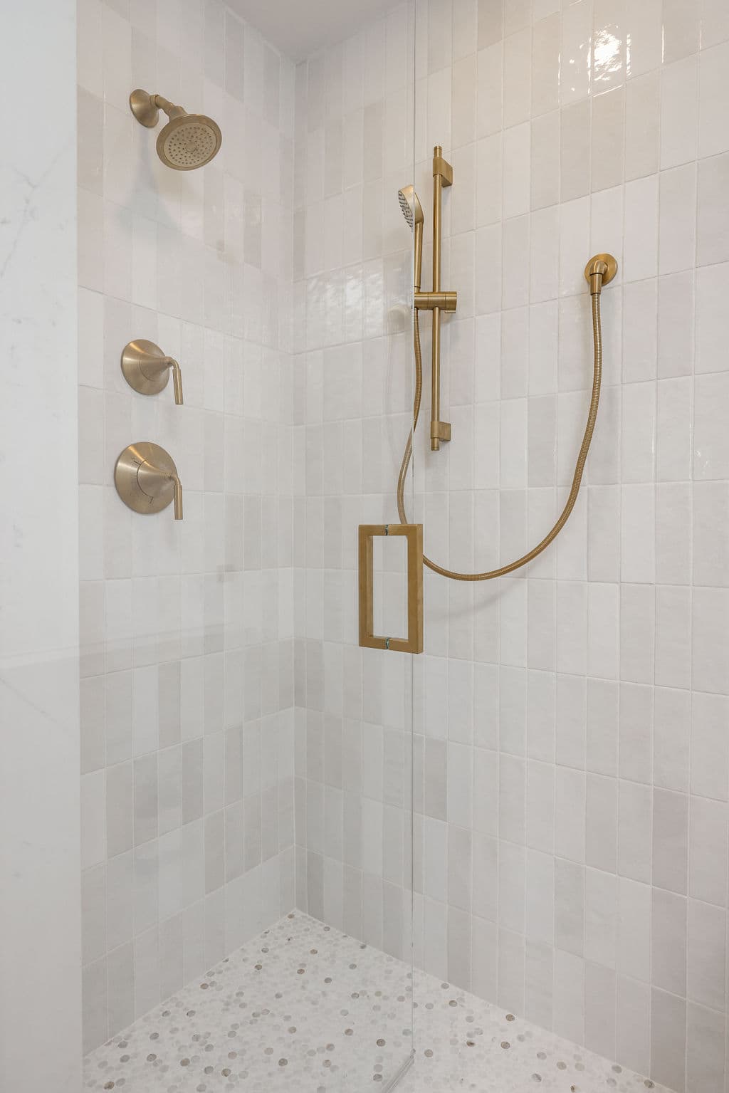Walk-in shower clad in marble tile with brass rainfall and handheld fixtures