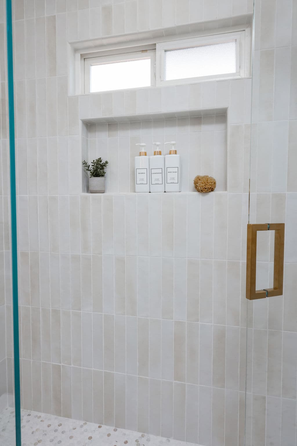 walk-in shower clad in vertical cream zellige tile with niche and brass door pull