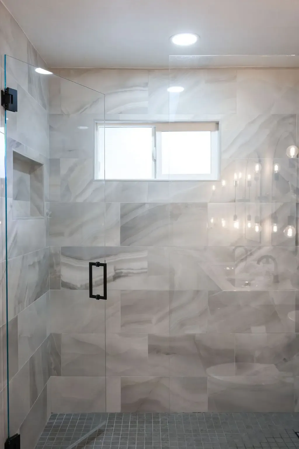 Walk-in shower clad in white marble-look tile with mosaic floor and glass enclosure