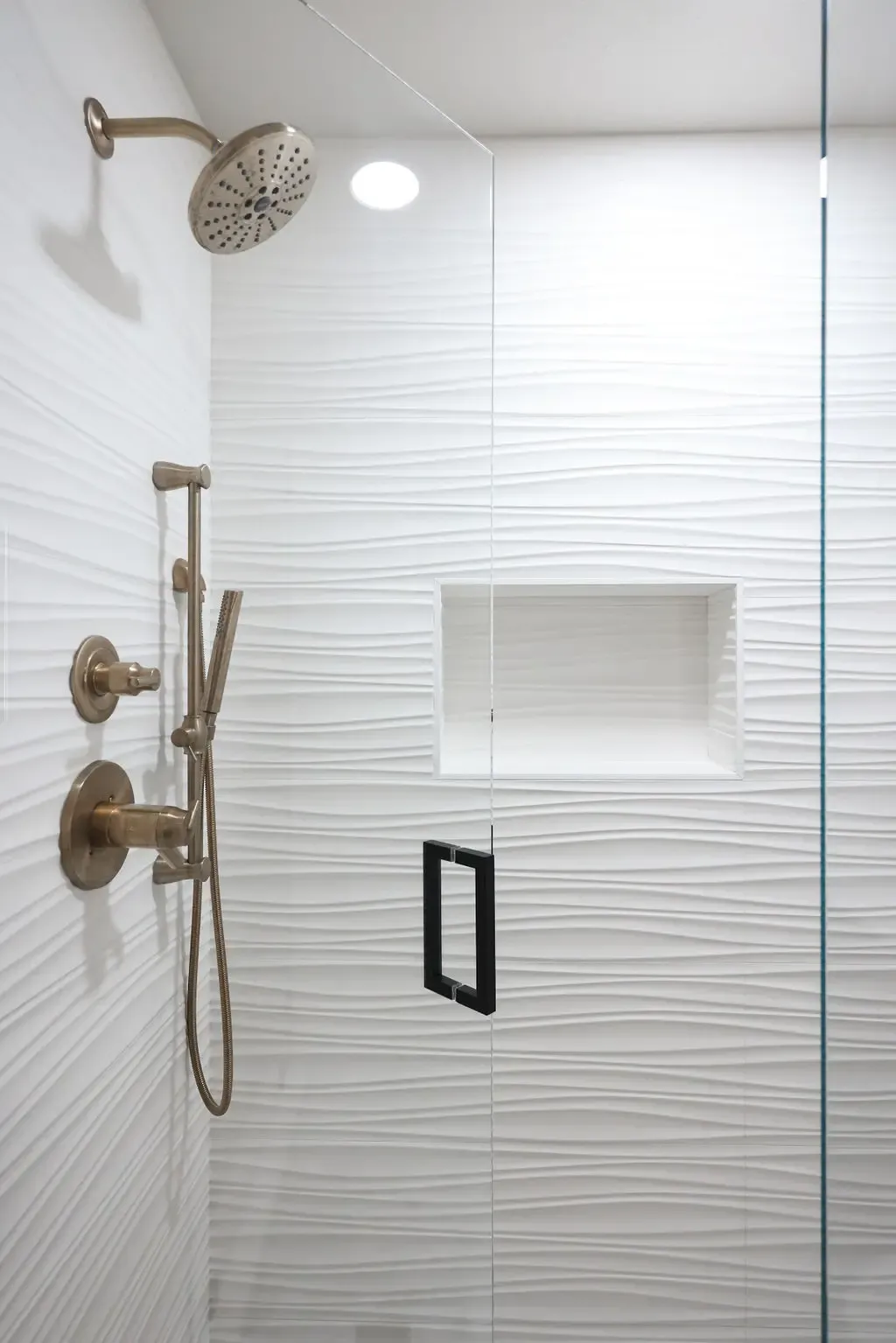 Walk-in shower clad in white wave-textured tile with brushed gold fixtures