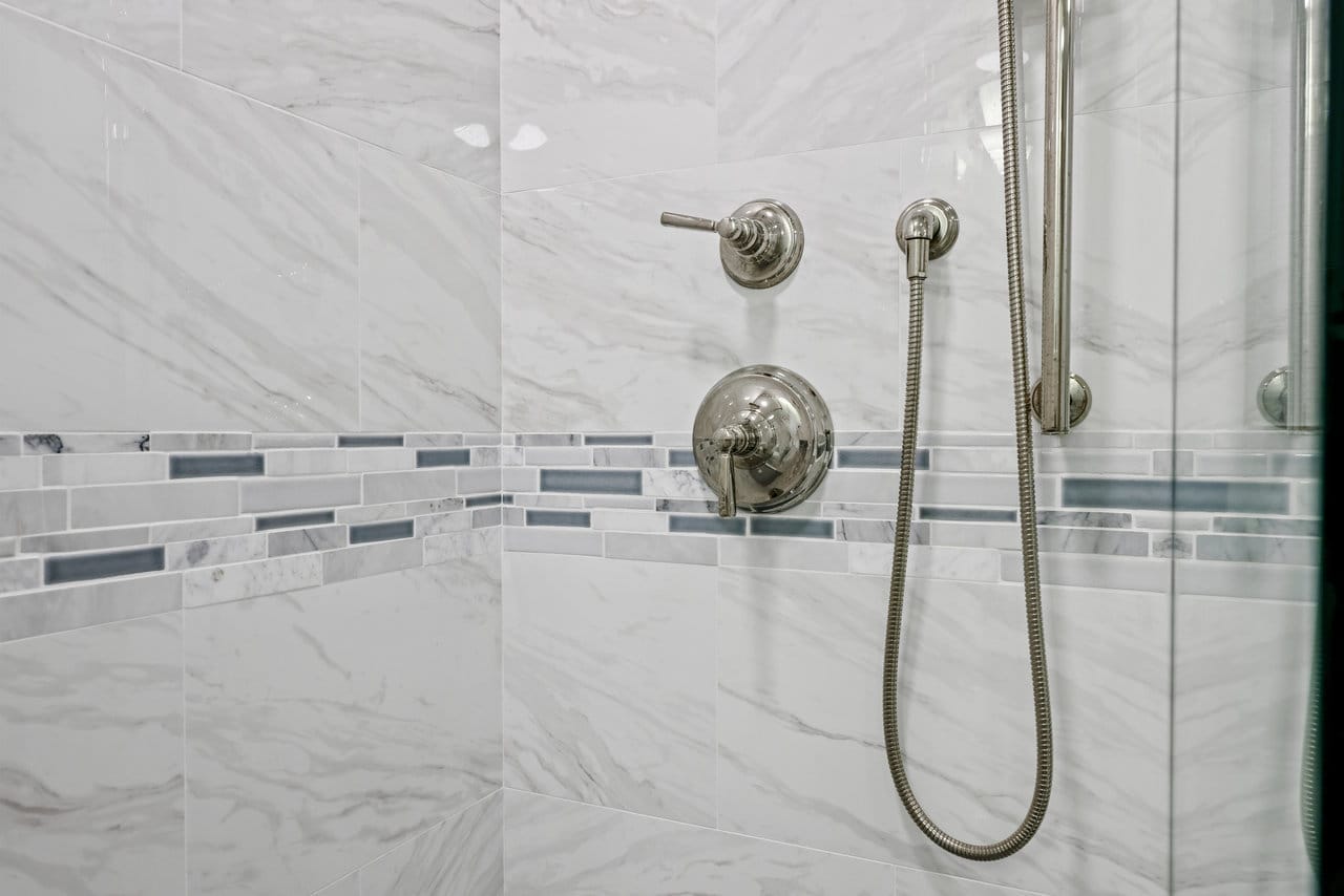 walk-in shower detail with polished chrome fixtures and marble tile glass mosaic stripe