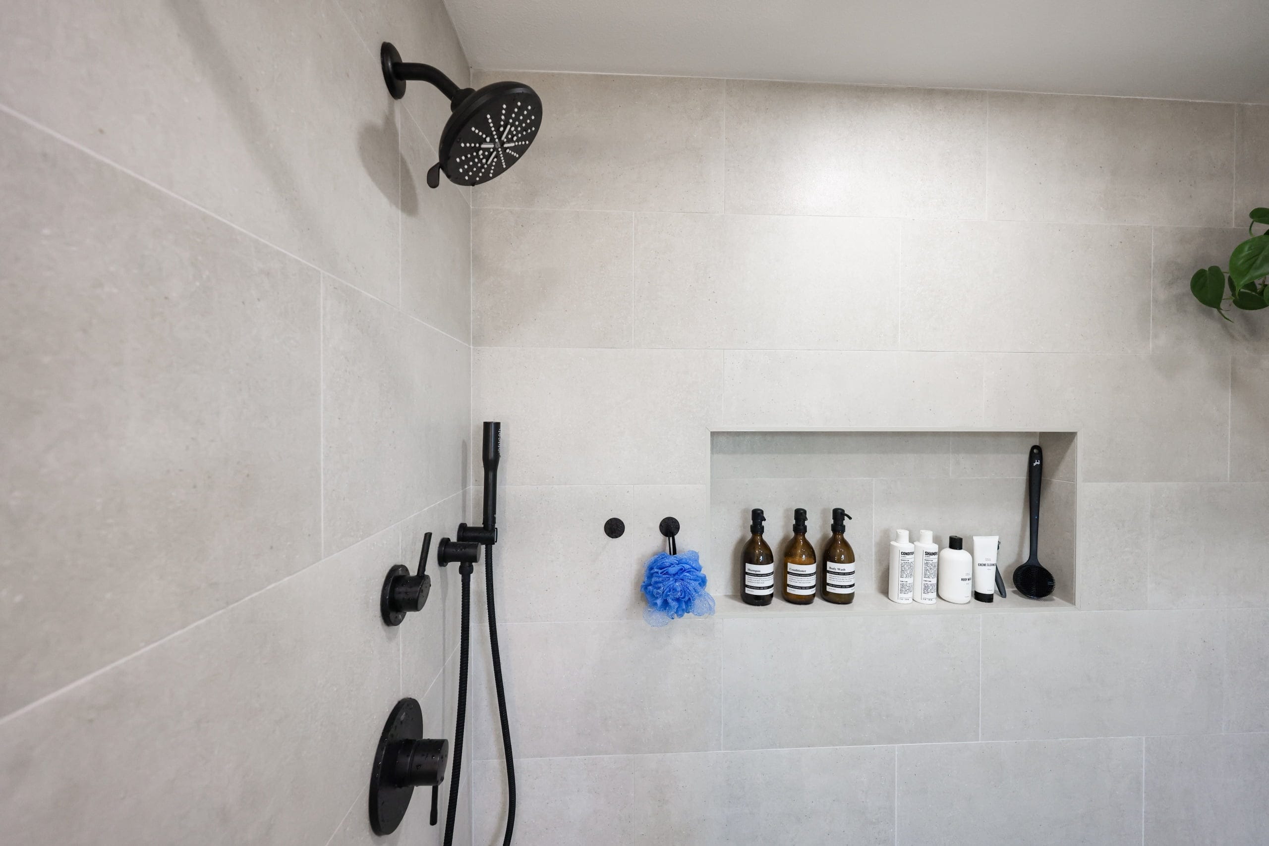 Walk-in shower in gray tile with black fixtures and recessed product niche
