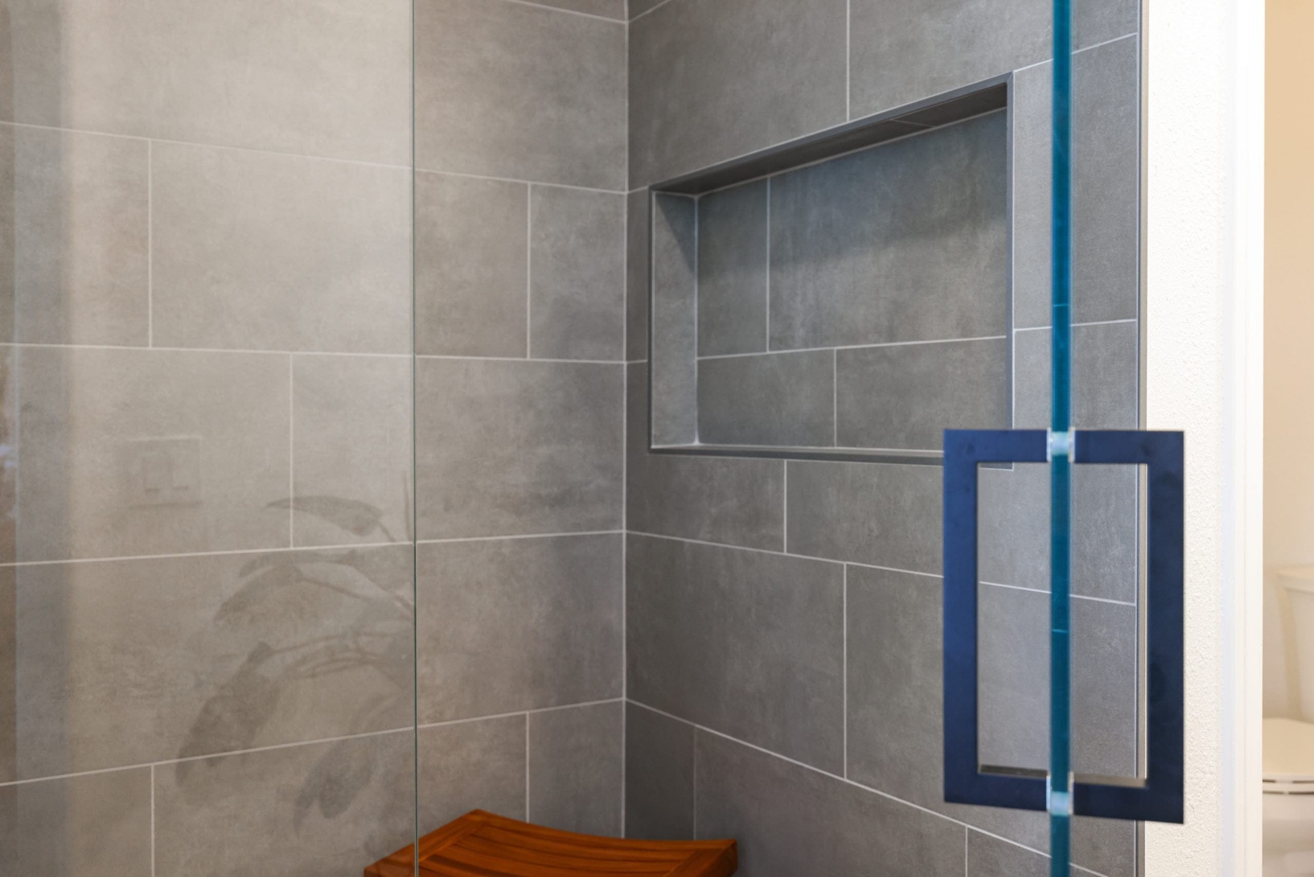 Walk-in shower with gray porcelain tile, recessed niche and teak corner stool