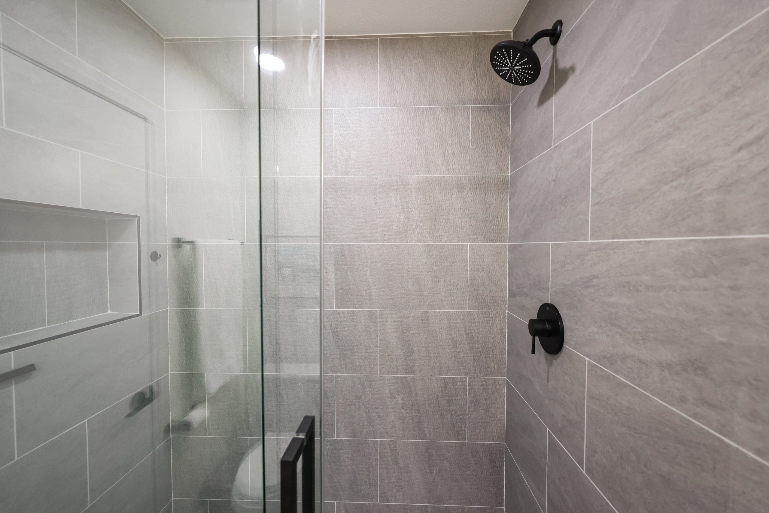 walk-in shower with gray wood-grain tile and matte black rainfall head