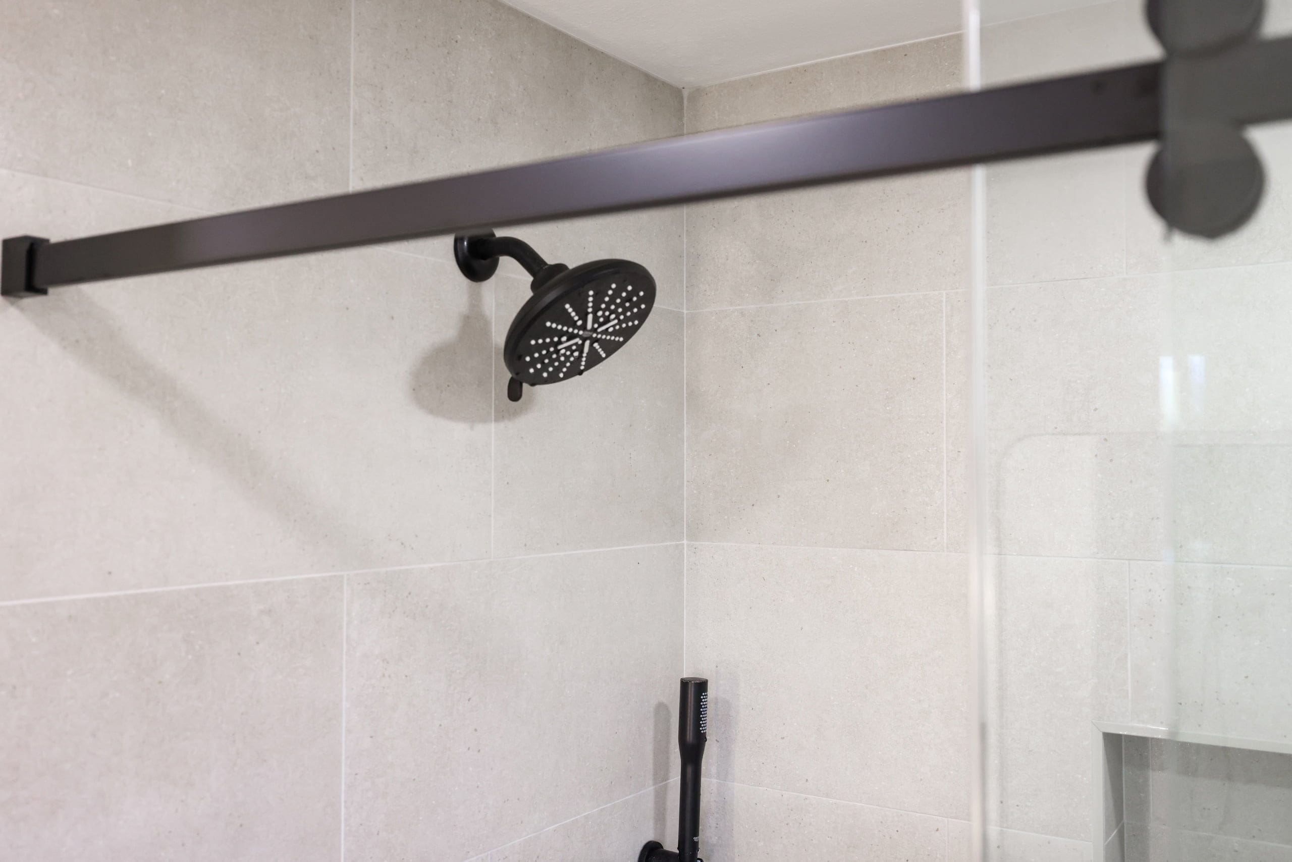 Walk-in shower with large beige tile and matte black rainfall showerhead