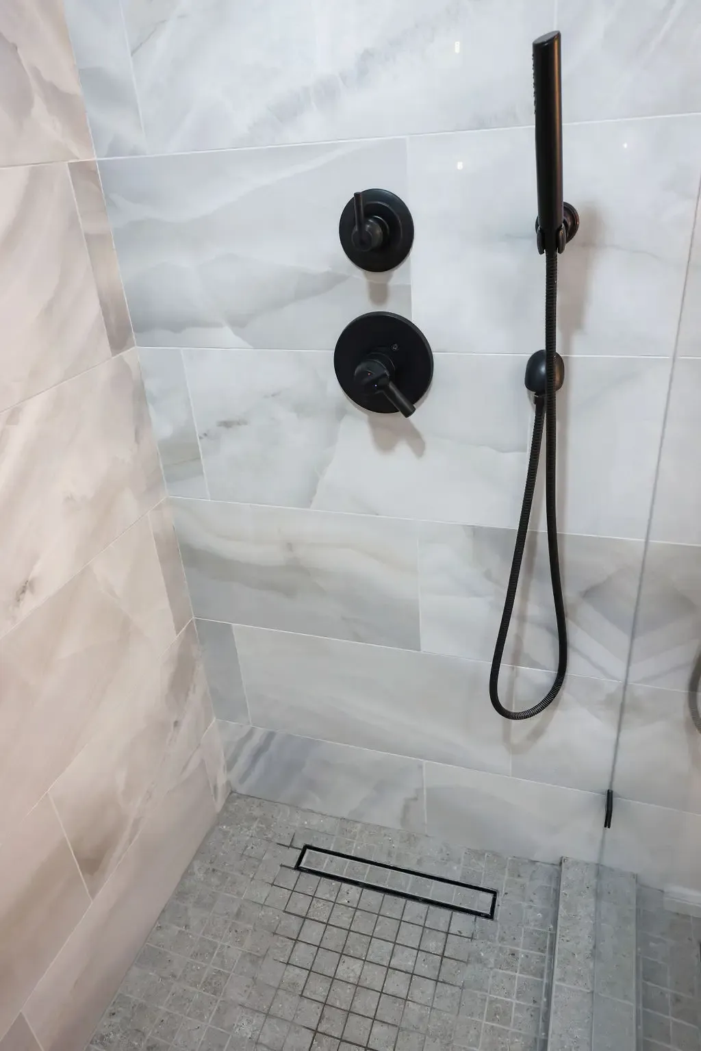 Walk-in shower with matte black hardware, marble tile and linear floor drain