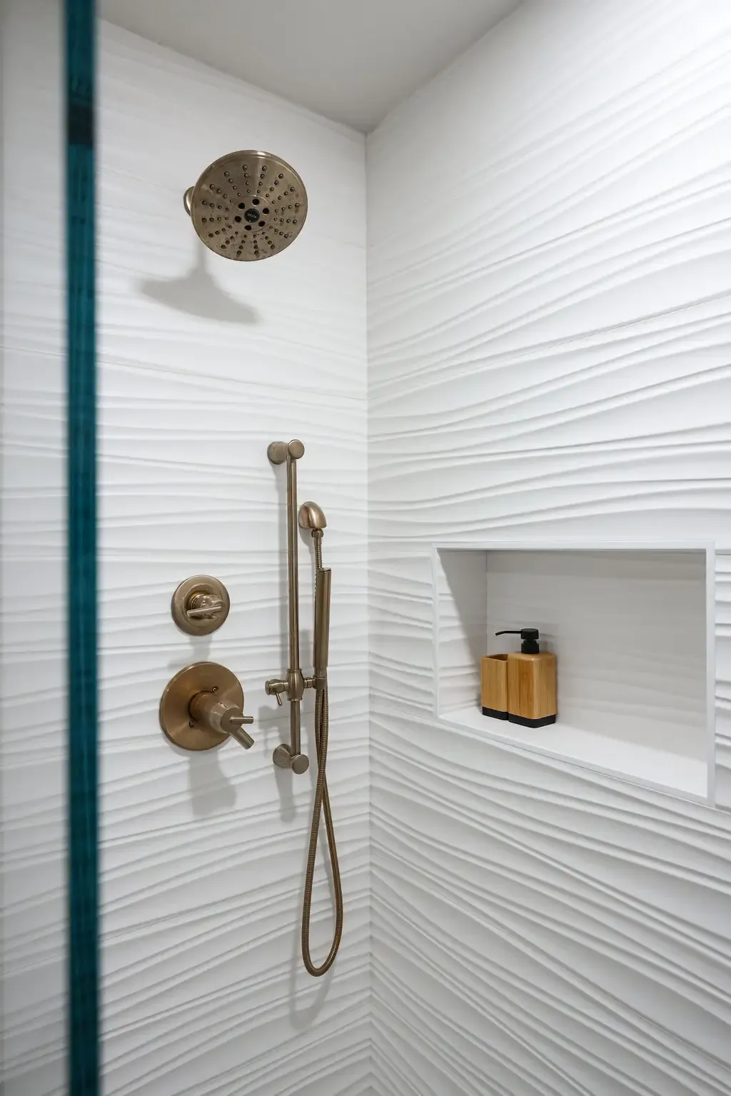 Walk-in shower with wavy white textured tile, bronze fixtures and recessed niche