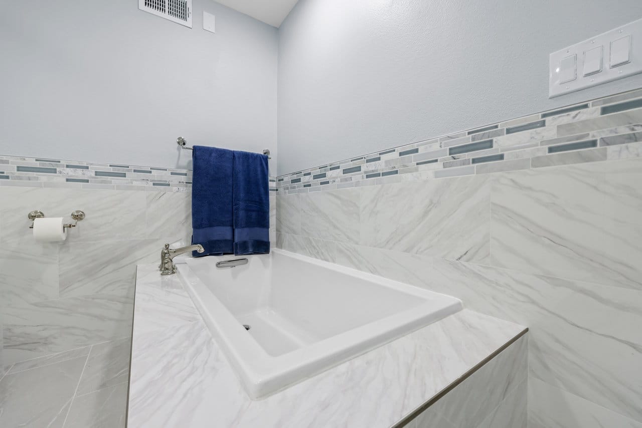 white drop-in soaking tub framed by marble tile and glass mosaic accent border