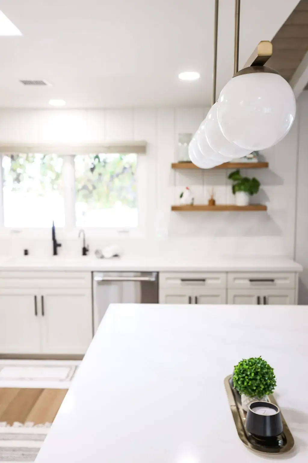 White quartz island and floating wood shelves in airy remodeled kitchen