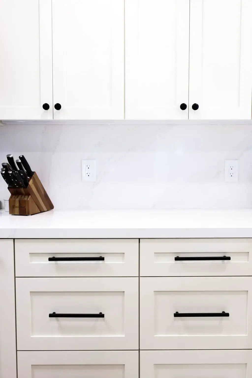 White shaker cabinets with matte black bar pulls and marble-look backsplash