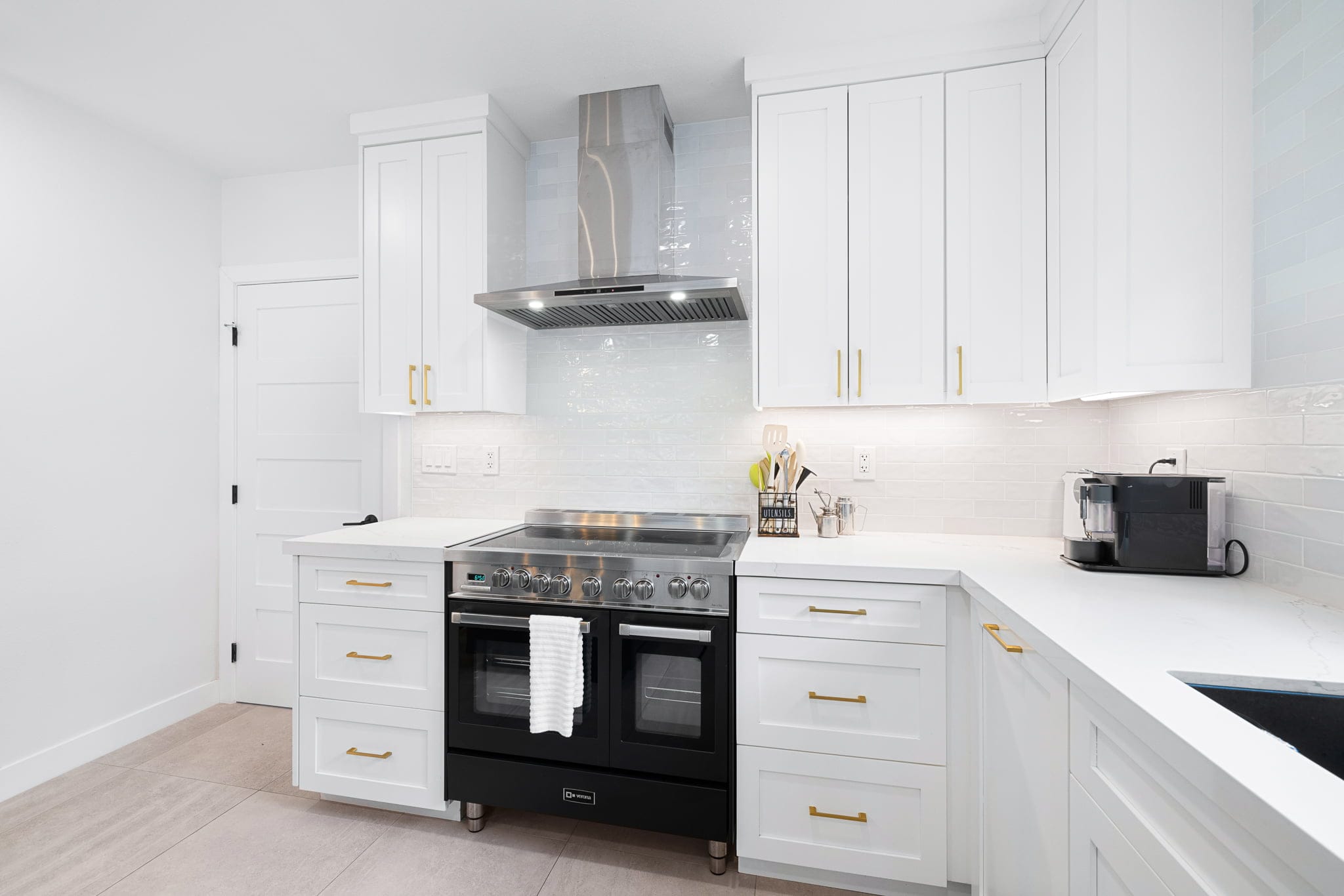 White shaker kitchen with quartz counters, gold pulls and stainless range hood