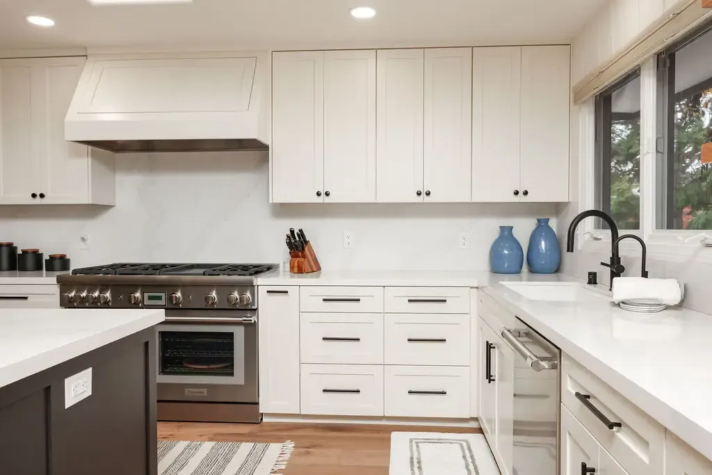 White shaker kitchen with quartz counters, pro gas range and black hardware