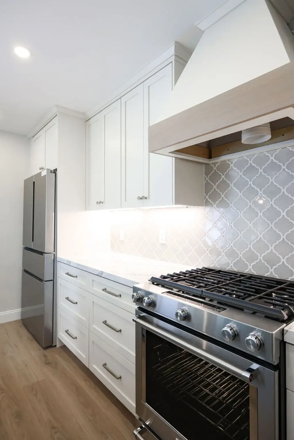 White shaker kitchen with stainless gas range, plaster vent hood, and counter-depth fridge
