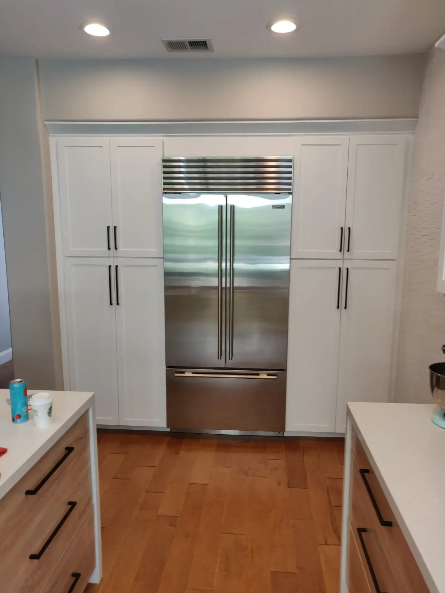 White shaker pantry cabinets flanking a stainless French-door refrigerator over wood floors