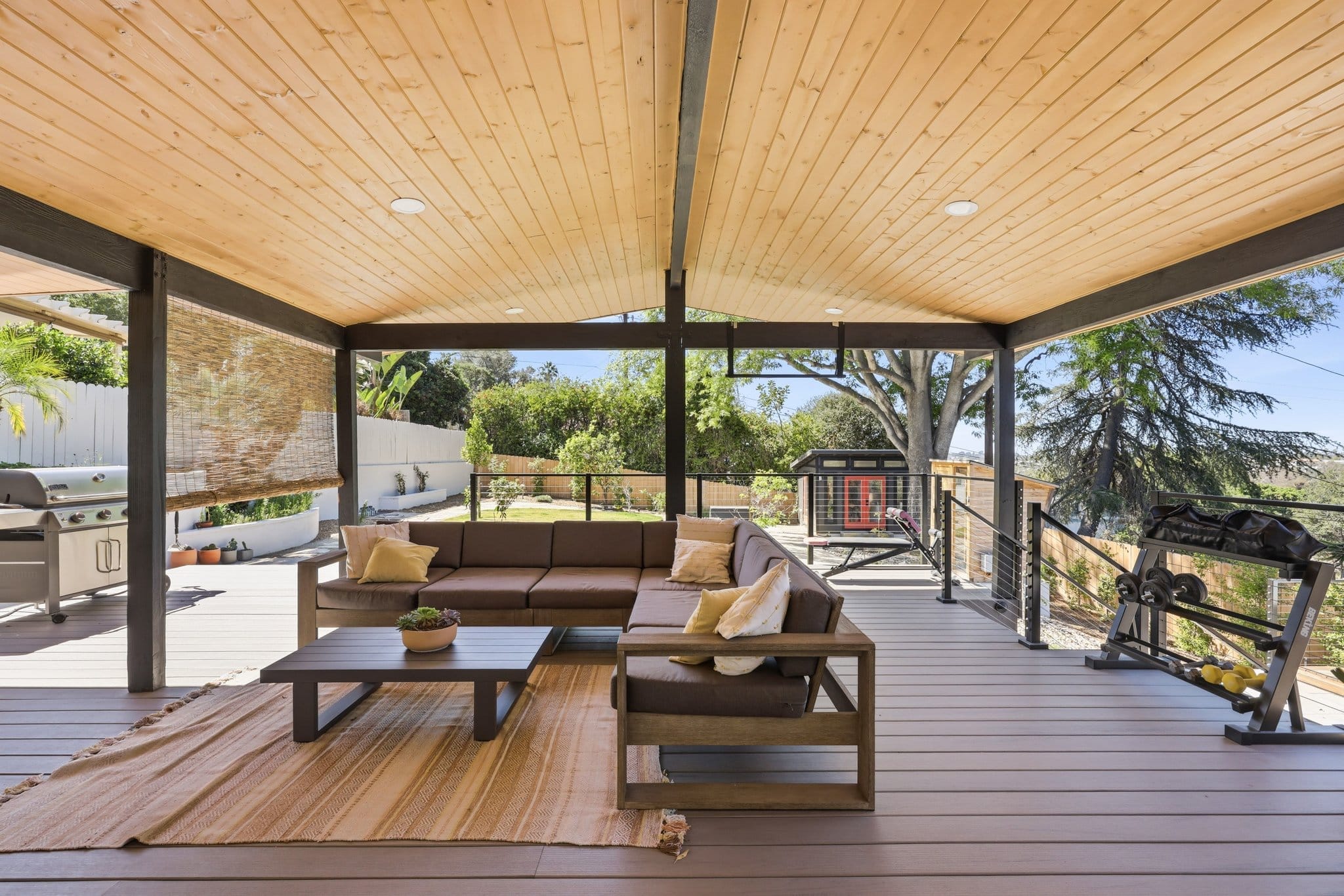 Covered backyard deck with wood ceiling, sectional sofa, grill and hillside view