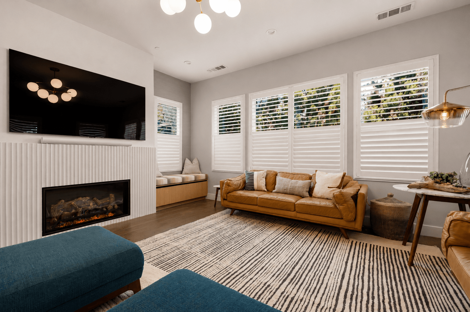Living room with linear fireplace, mounted television and tan leather sofa under shuttered windows
