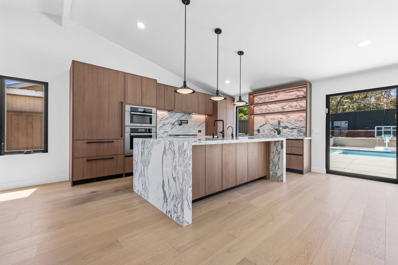 Open modern kitchen with walnut cabinets, marble waterfall island, and pool-view sliders