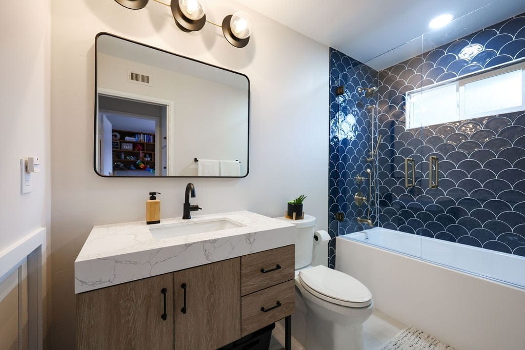 Bathroom vanity with quartz counter, wood cabinet and navy fish-scale tile tub surround