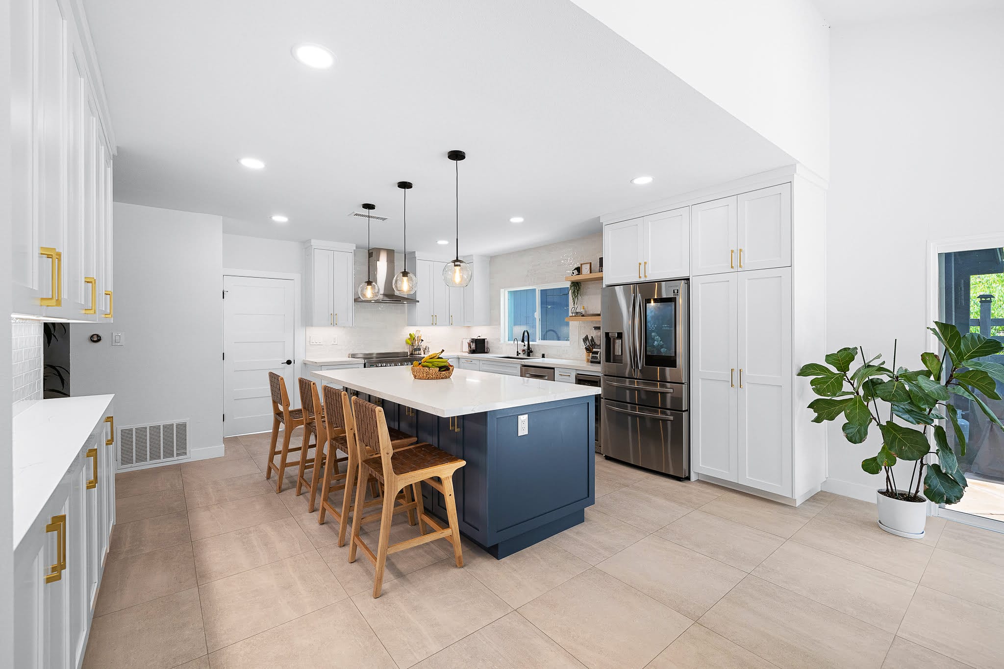 Bright open kitchen with navy island, white shaker cabinets, and brass hardware