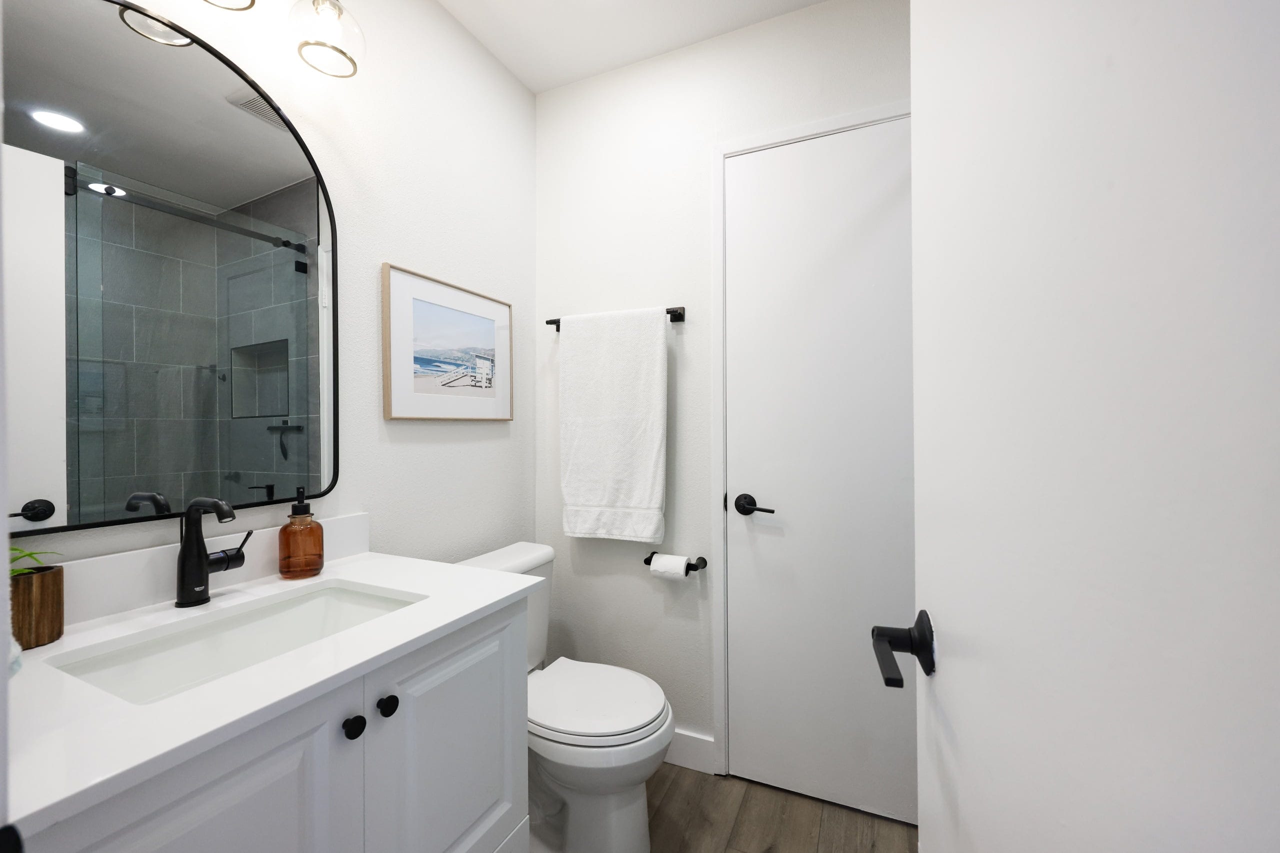 compact powder room with white vanity, arched mirror and coastal art