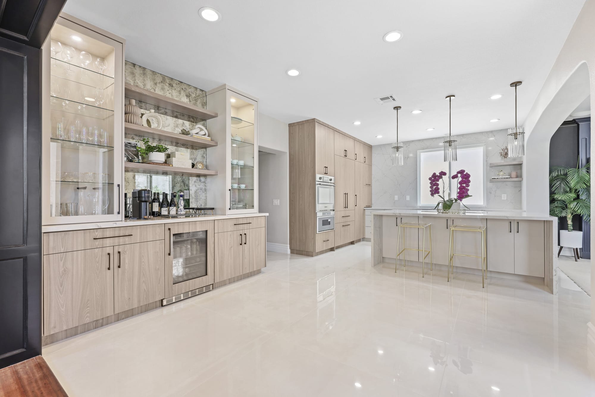 Spacious modern kitchen with pale wood cabinetry, marble backsplash, island and glossy tile floor