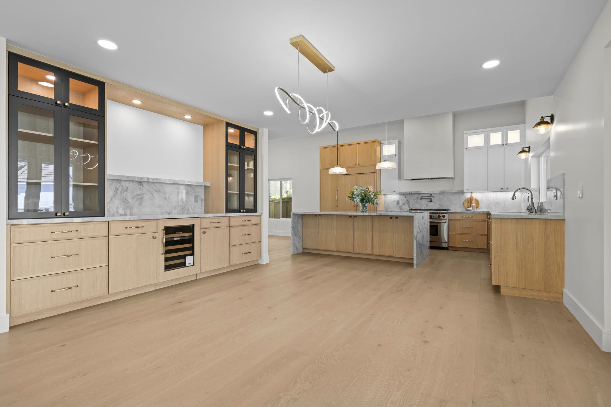 Spacious modern kitchen with light oak cabinets, marble counters and ring chandelier