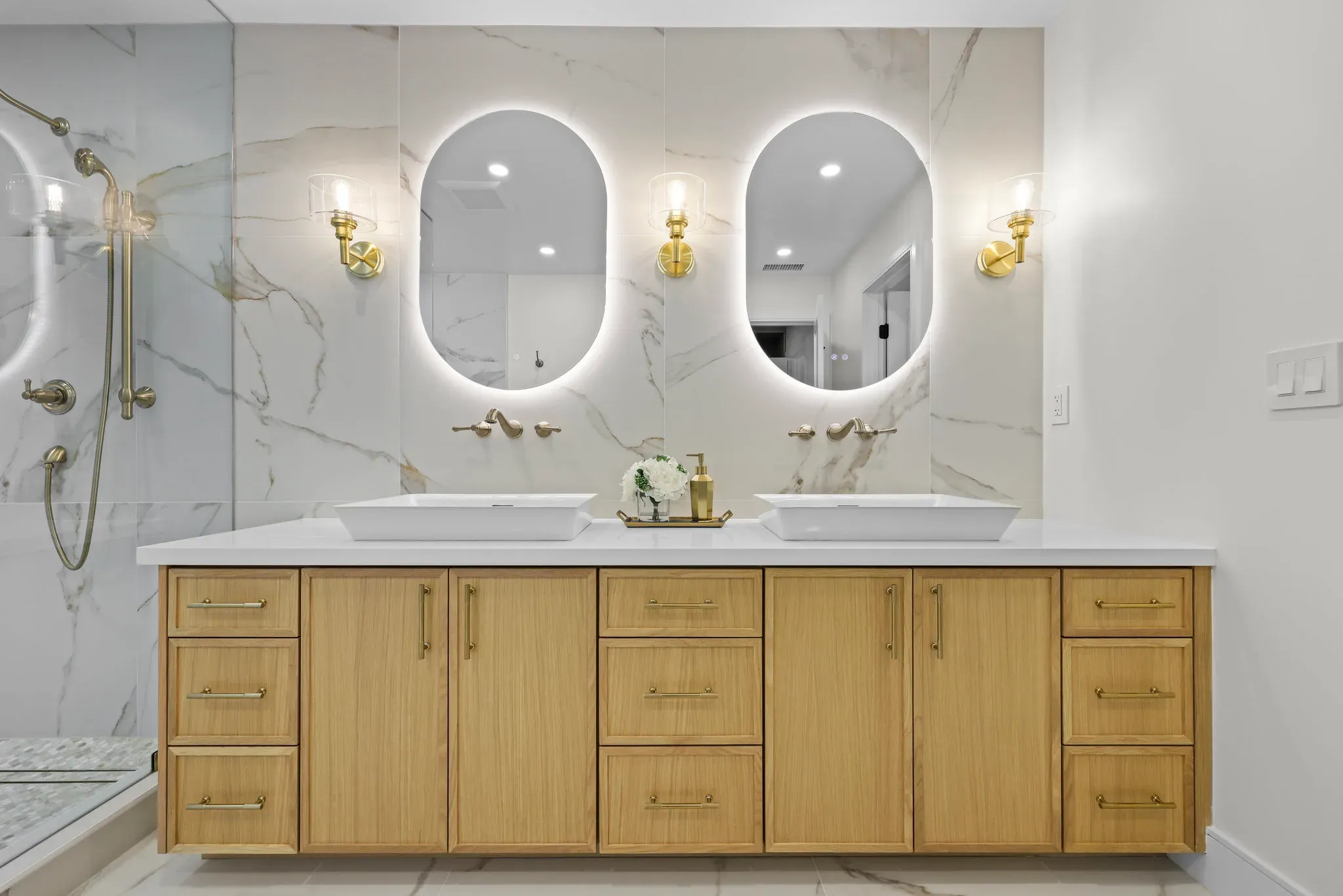 Luxury bathroom remodel with marble slab walls, floating oak vanity, and backlit oval mirrors