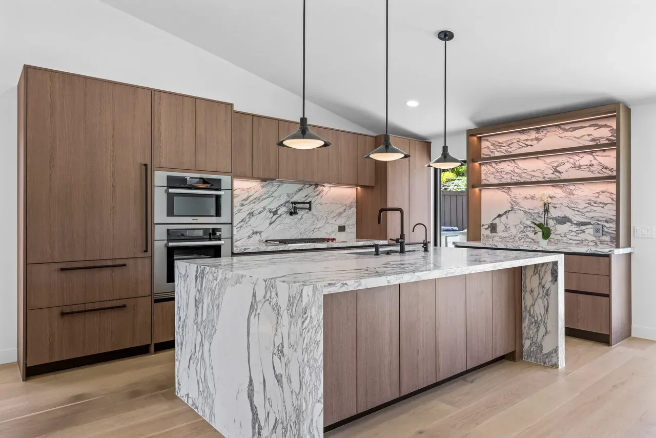 Modern kitchen remodel with wood cabinetry, marble waterfall island, and double wall ovens