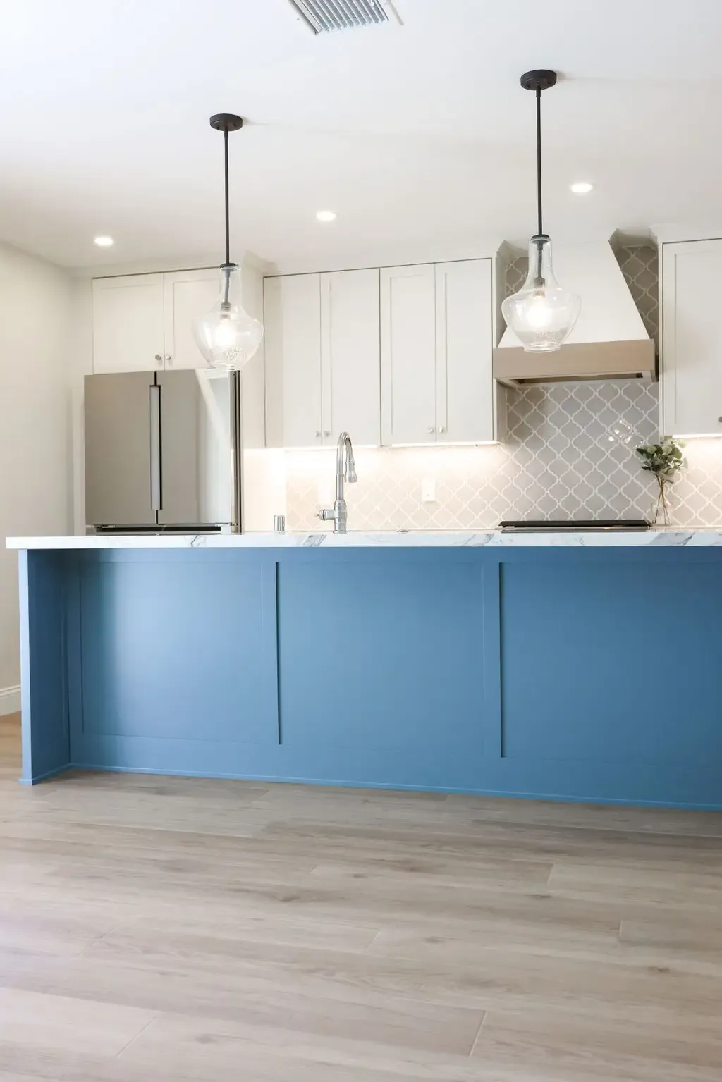 Modern kitchen with blue shaker island, white cabinets and pendant lights over light wood floor