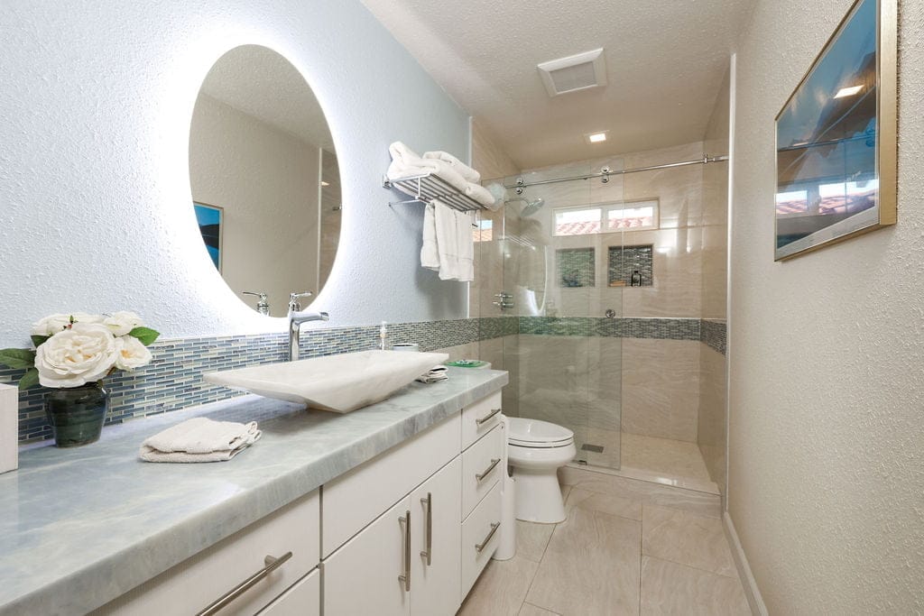 narrow bathroom with white vanity, oval mirror and tiled walk-in glass shower