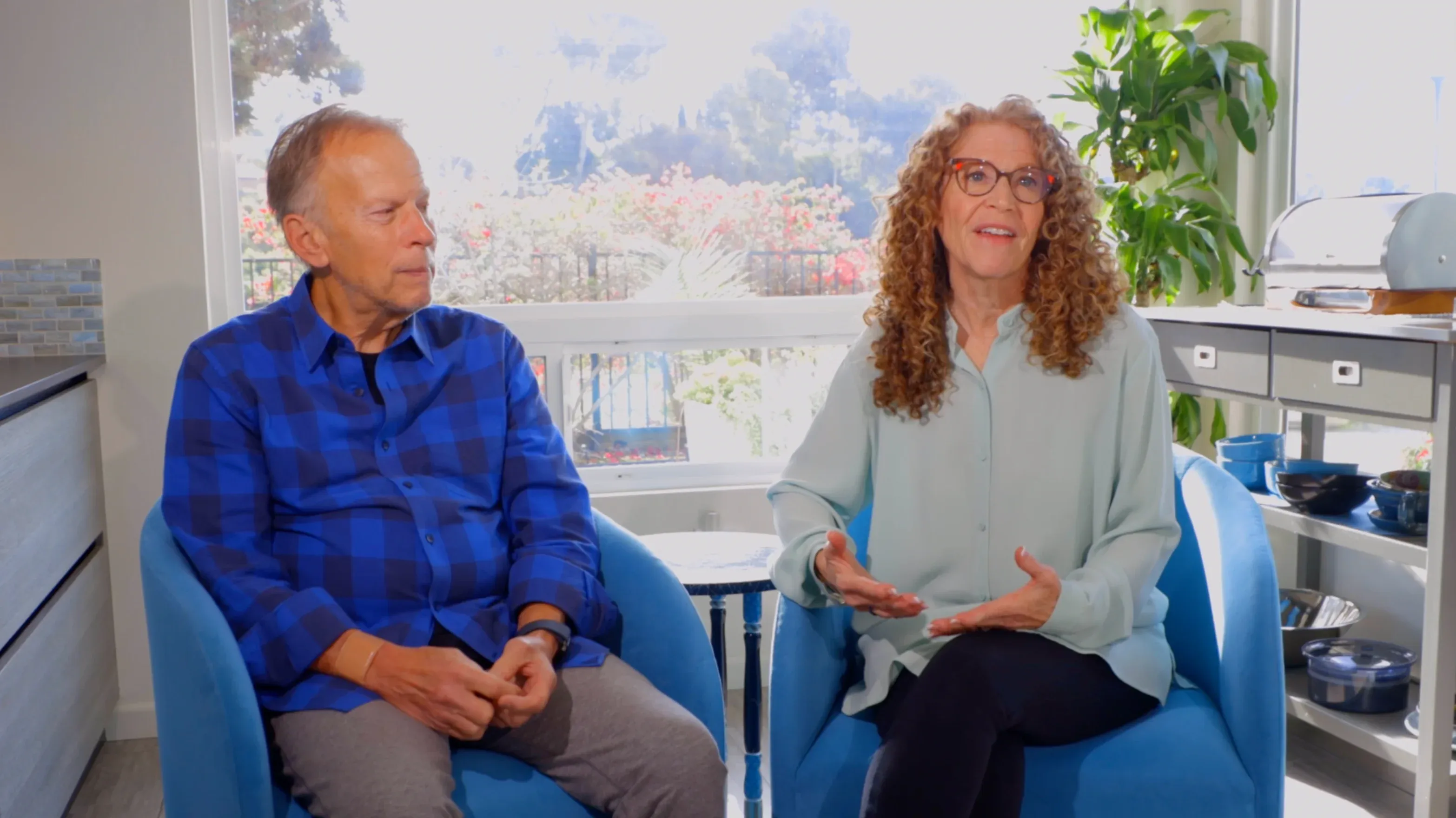 Older couple seated in bright sunroom with blue armchairs and ocean view