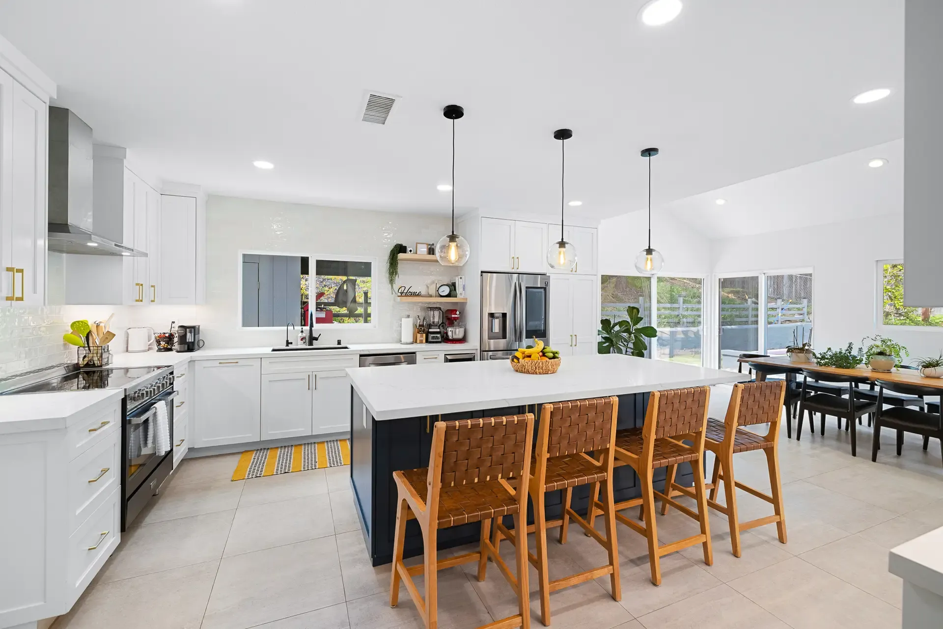 Open-concept white kitchen remodel with navy island, quartz counters, and woven leather barstools