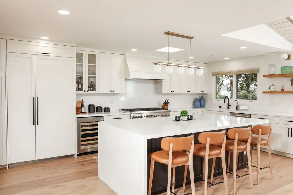 Open-plan white kitchen with waterfall island, leather barstools and skylight