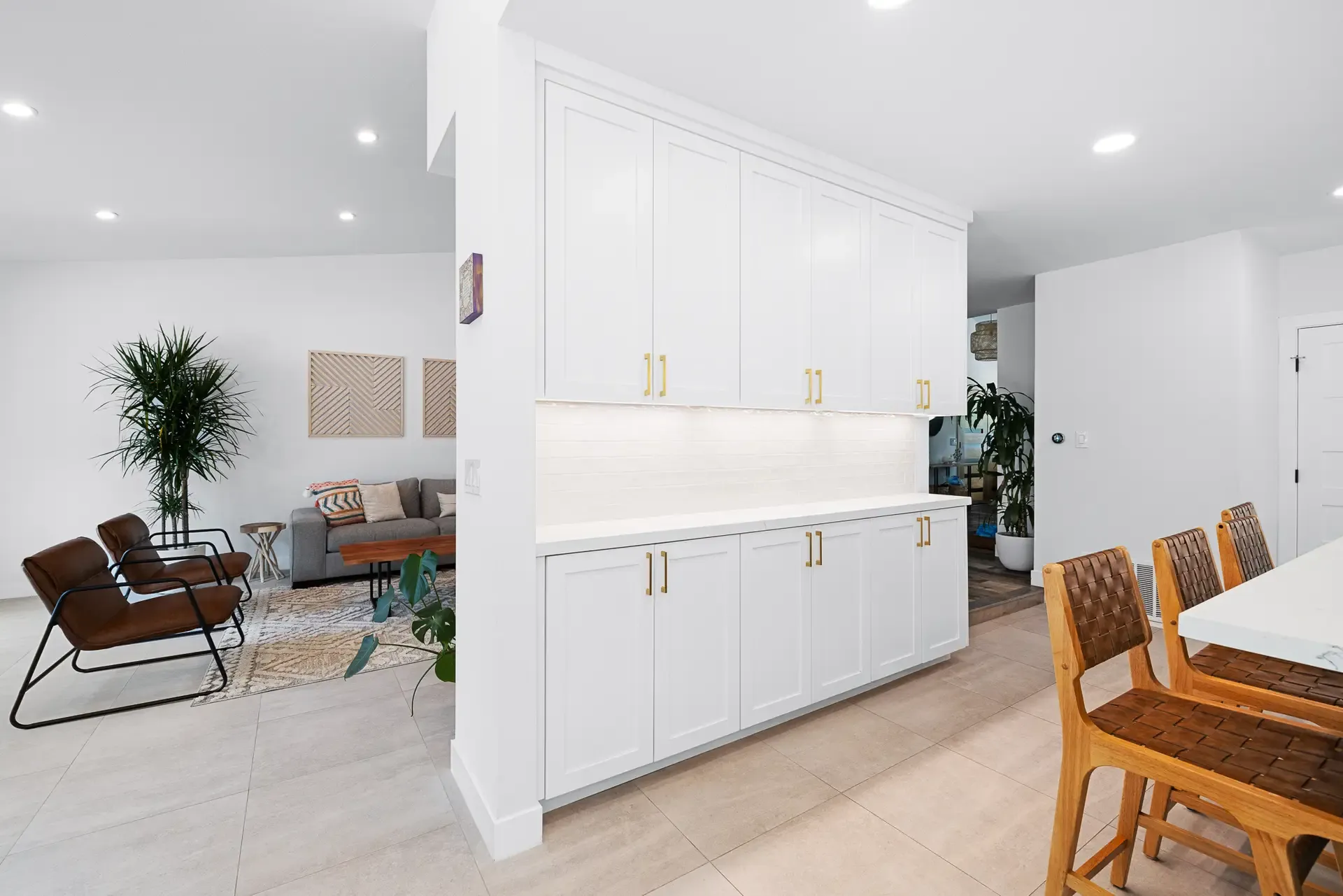 White built-in cabinetry with brass pulls dividing open dining and living area on tile floor
