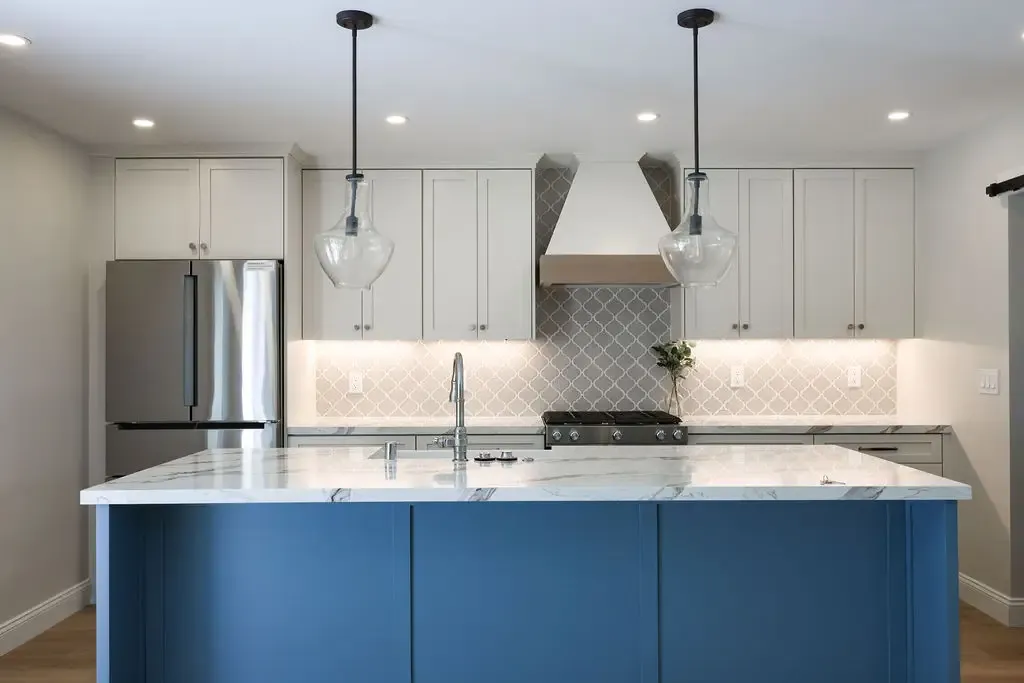 Contemporary kitchen with deep blue island, marble counters and arabesque tile backsplash