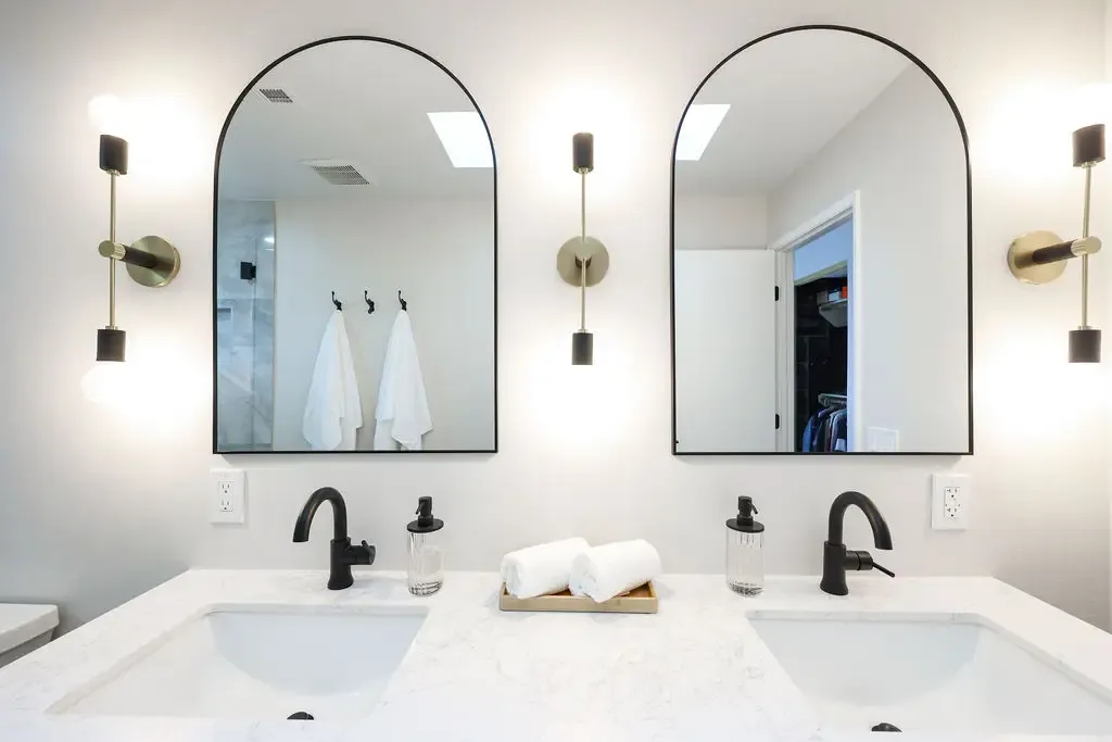 Modern bathroom with double quartz vanity, arched mirrors and black brass fixtures