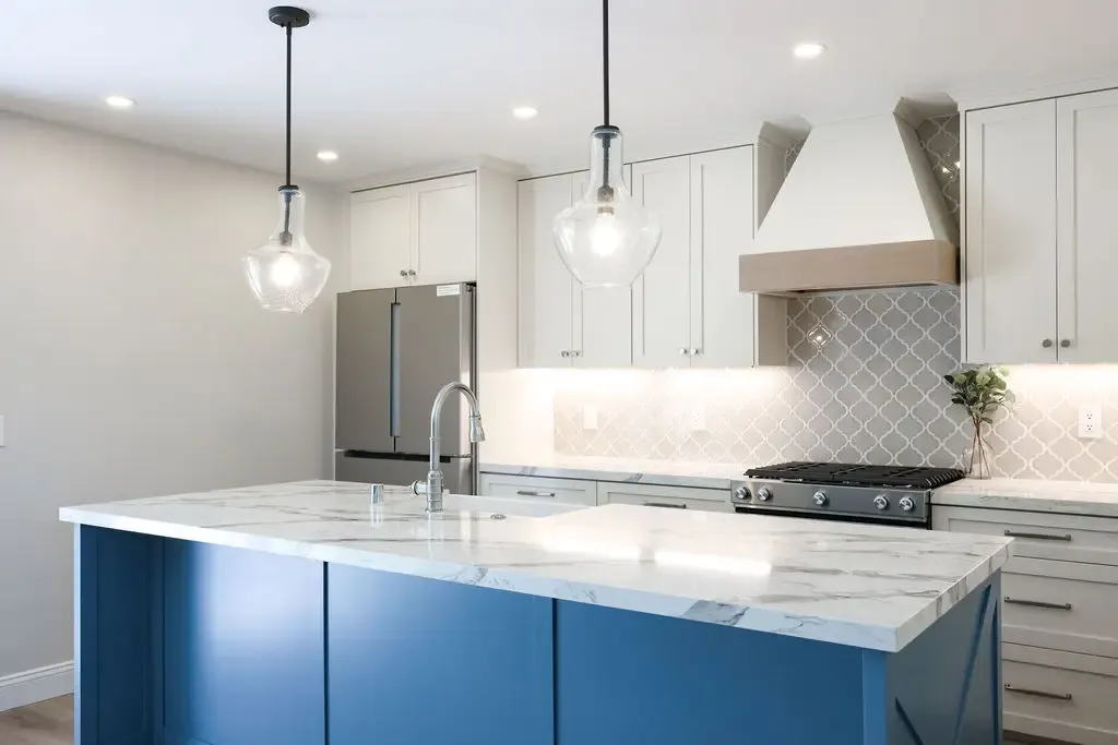Open kitchen featuring blue waterfall island, marble counters, and glass pendant lights
