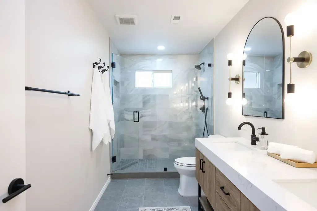 Remodeled bathroom with glass walk-in shower, marble tile, and floating wood vanity